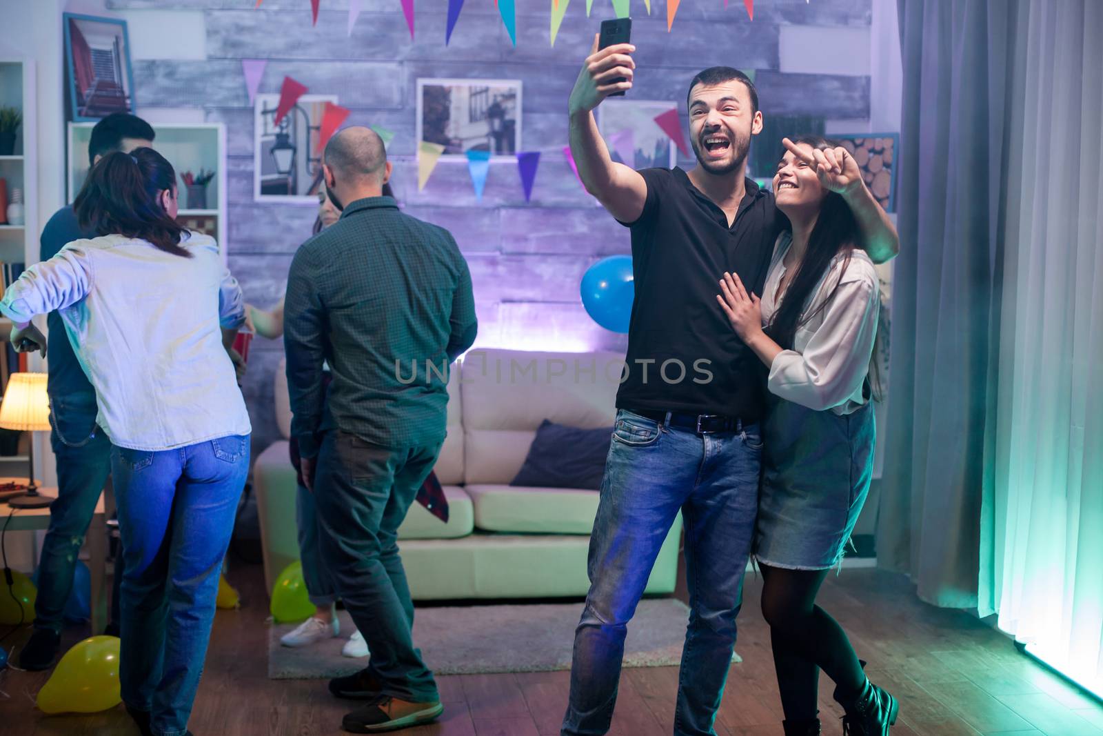 Group of young people dancing at a party while man and woman taking a selfie.