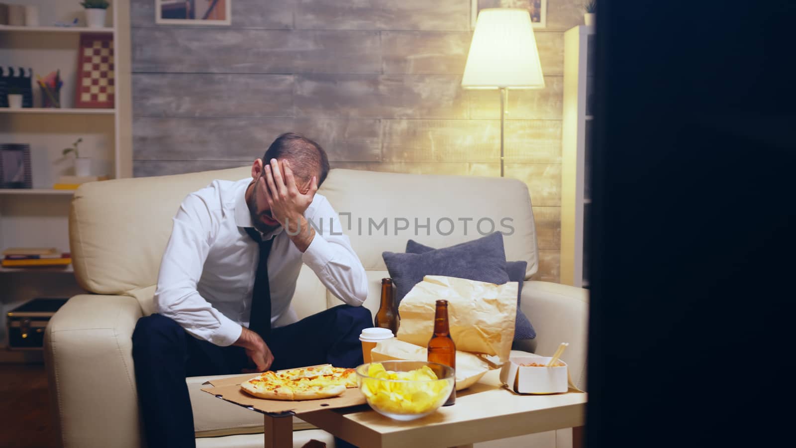 Revealing shot of businessman in suit watching a game after work sitting on couch.
