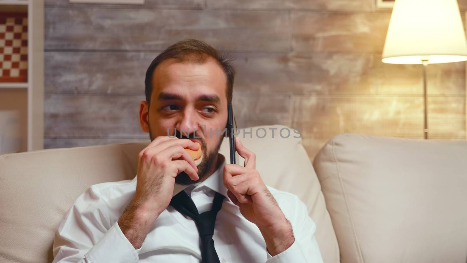 Young entrepreneur in formalwear eating a burger while having a business conversation on the phone.