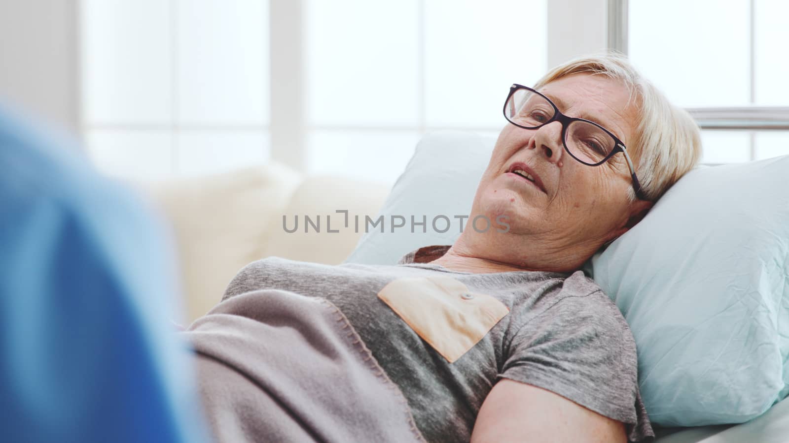 Close up of old sick woman lying in bed talking with a male assistant, over the shoulder shot