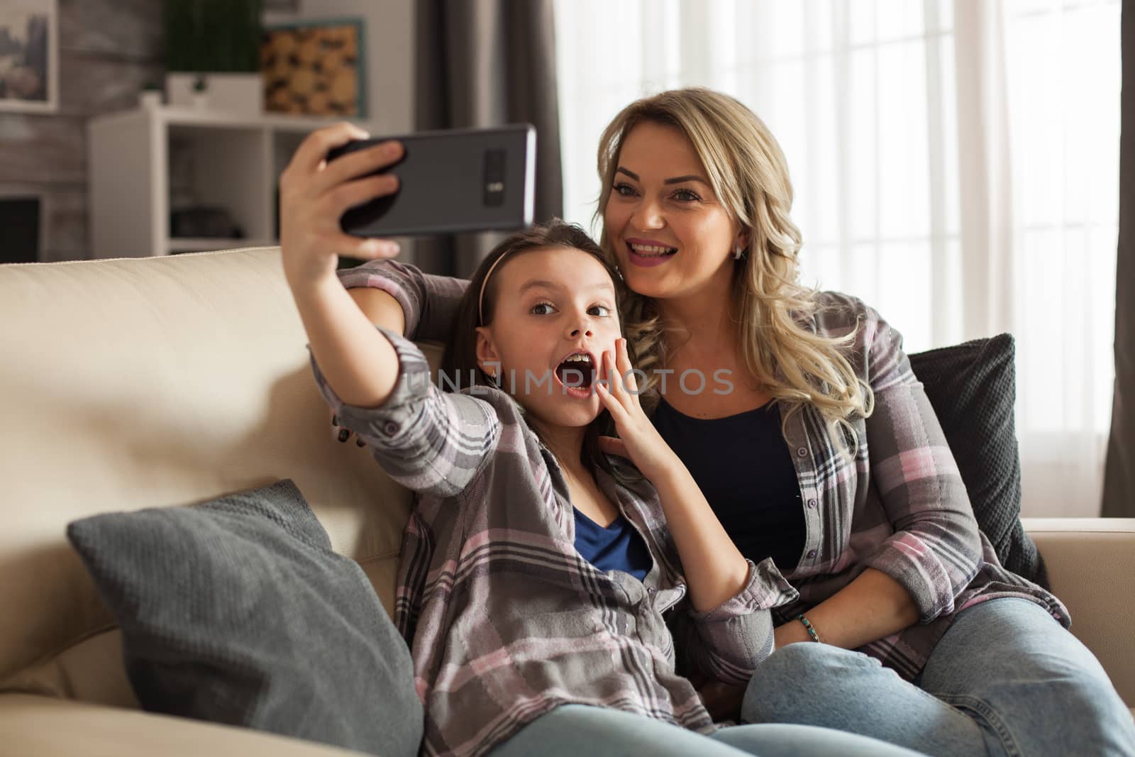 Excited daughter taking a selfie with her mother using her smartphone. Happy kid.