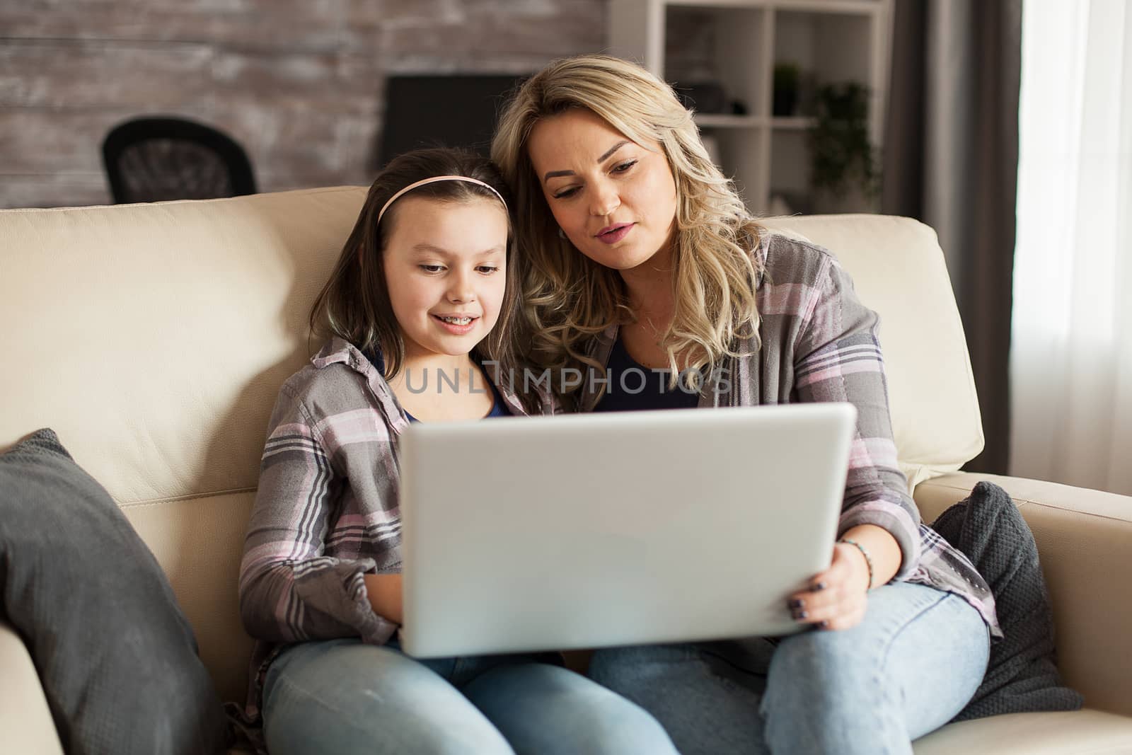 Mother and daughter sitting on the couch in living room watching a movie on laptop.