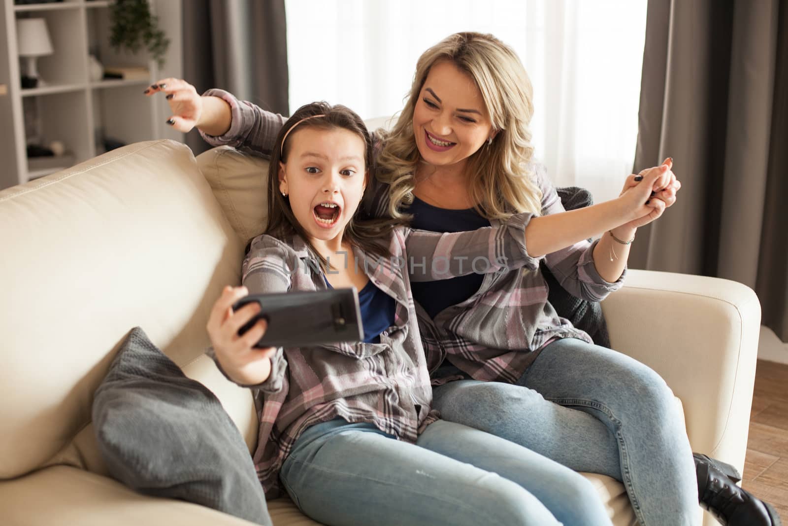 Attractive young mother and her little daughter using smartphone to take a selfie for her husband.