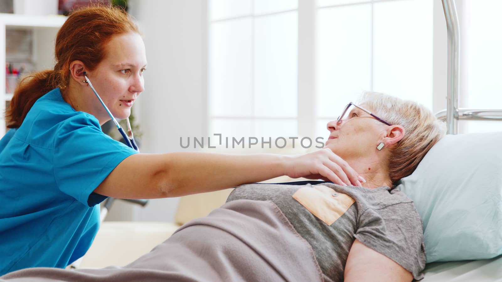 Old lady getting her heartbeats checked by a female nurse in bright and cozy nursing home