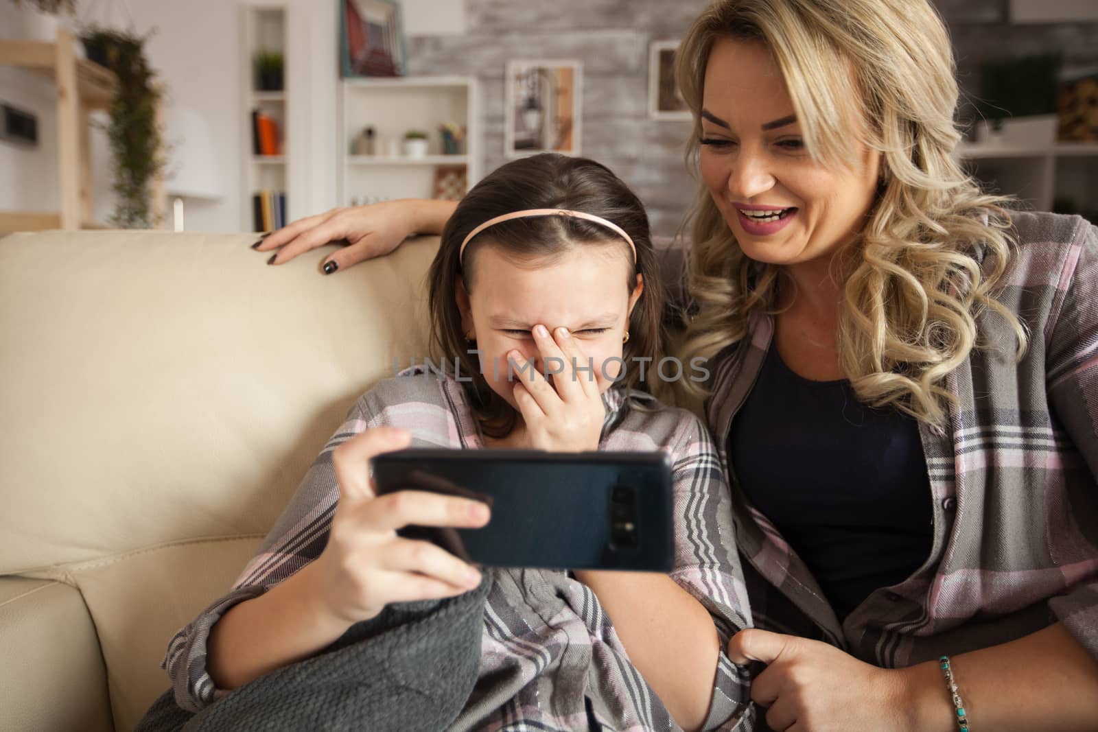 Amused preschool girl while using smartphone sitting on the couch with her mother.