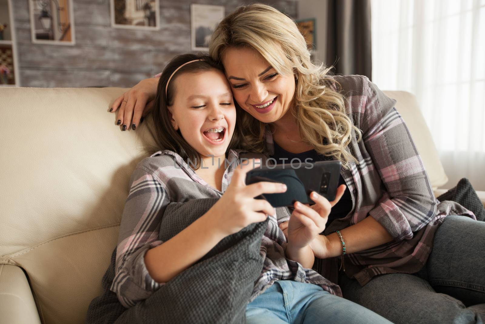 Young mother helping her little daughter with braces to use the apps from smartphone sitting on the couch in their apartment.