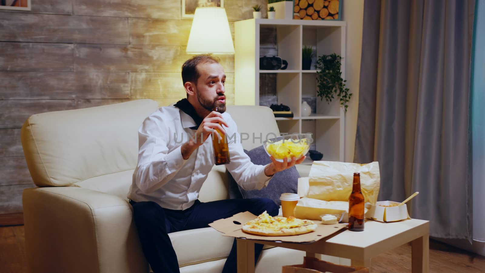 Tired and excited entrepreneur with tie eating chips and watching sports on tv.