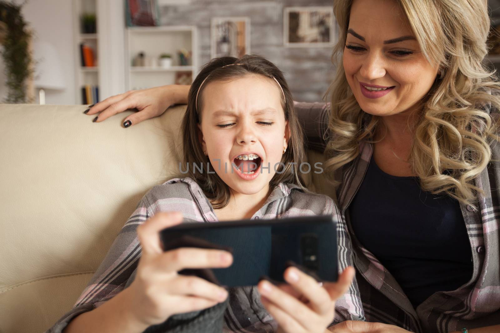 Little girl with braces and her mother sitting on the couch in living room watching cartoon on living room.