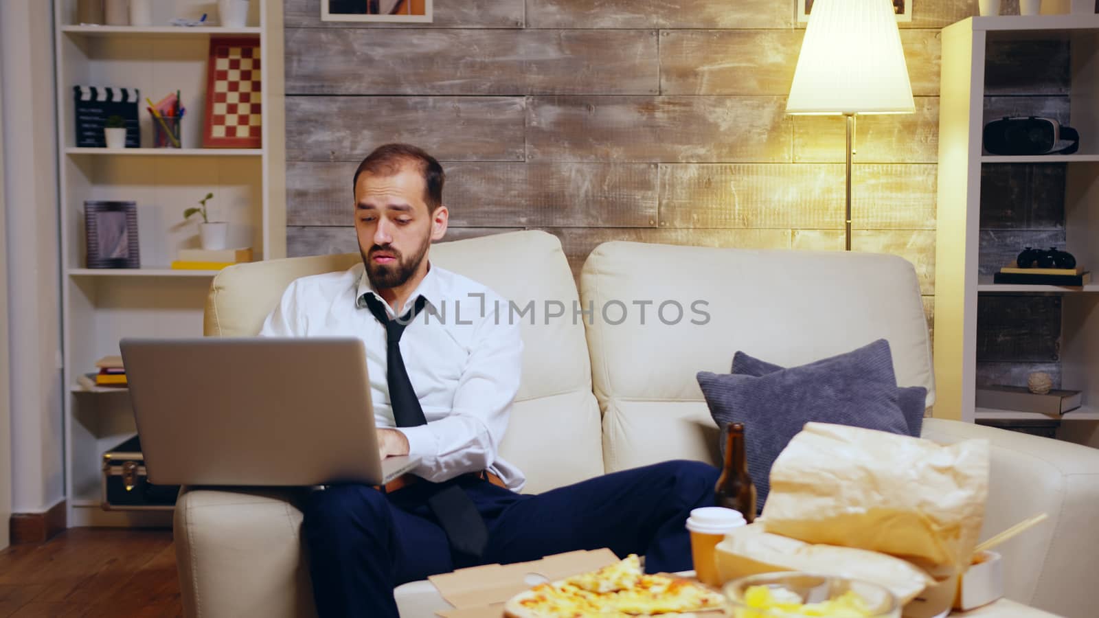 Businessman reaching out for his beer while working on laptop from home. Entrepreneur in suit.