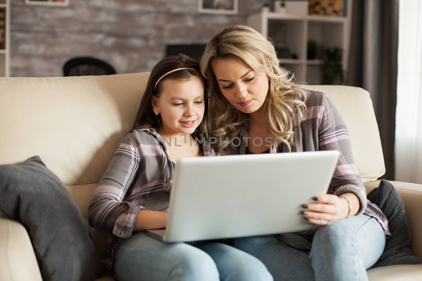 Modern mother and daughter sitting on the couch on a lazy weekend browsing on computer.