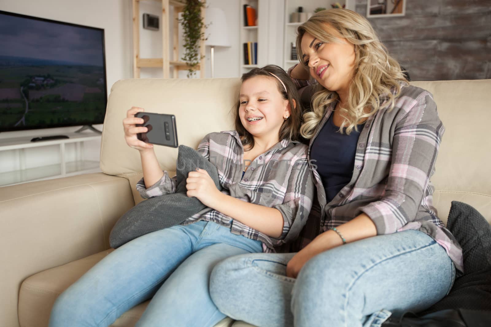 Mother and daughter with matching clothes sitting on the couch watching a funny video on smartphone.