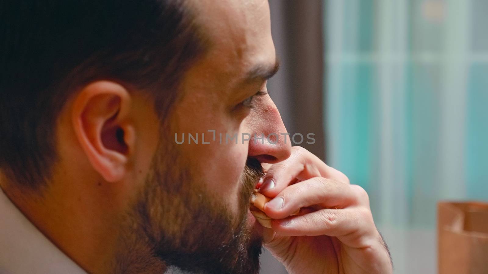 Close up of businessman biting from a burger in living room. Tasty fast food.