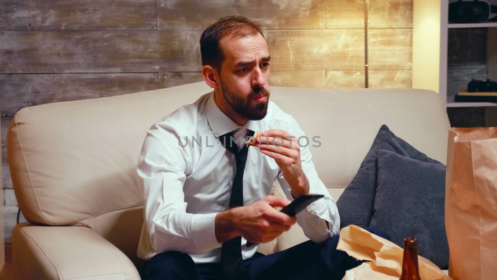 Businessman with tie eating a burger while watching tv. Hungry man.