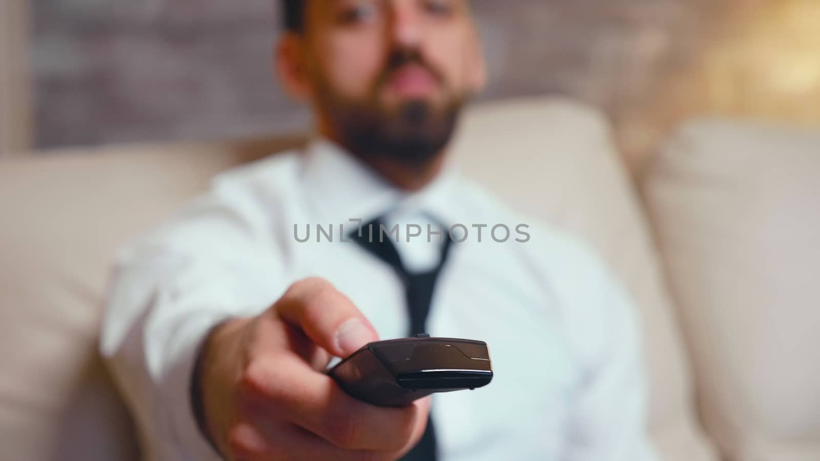 Close up of businessman using tv remote control while resting in living room.