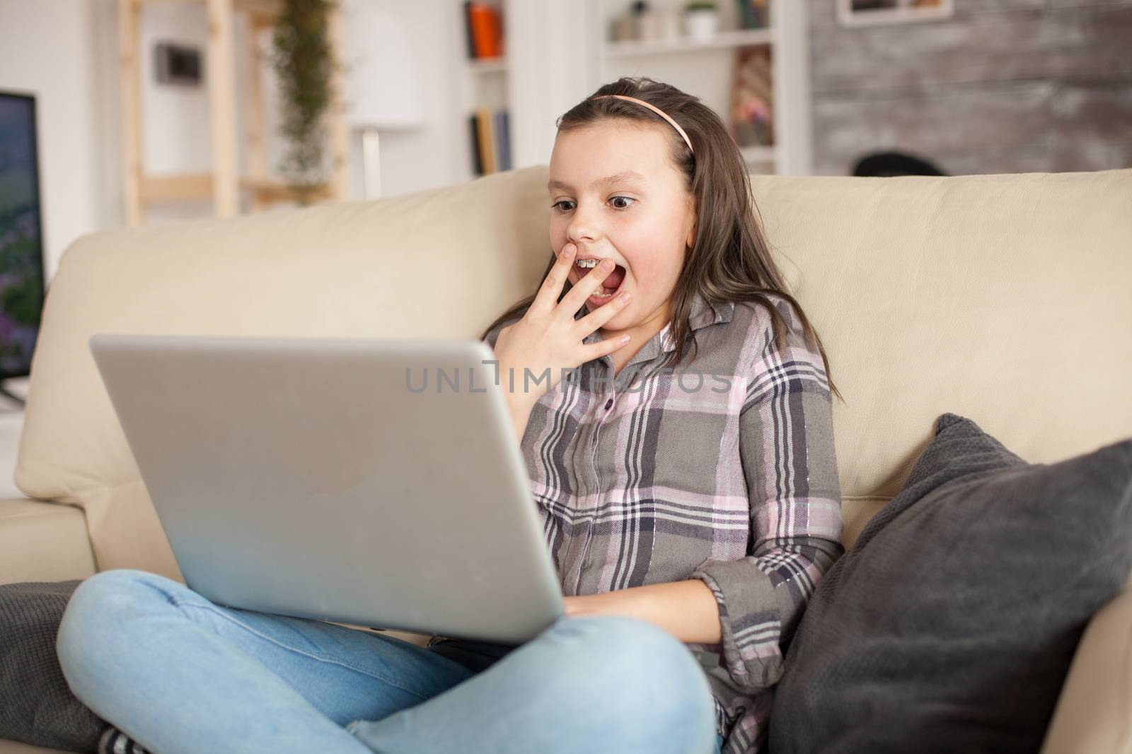 Excited little girl with braces while using her laptop sitting on the couch in living room.