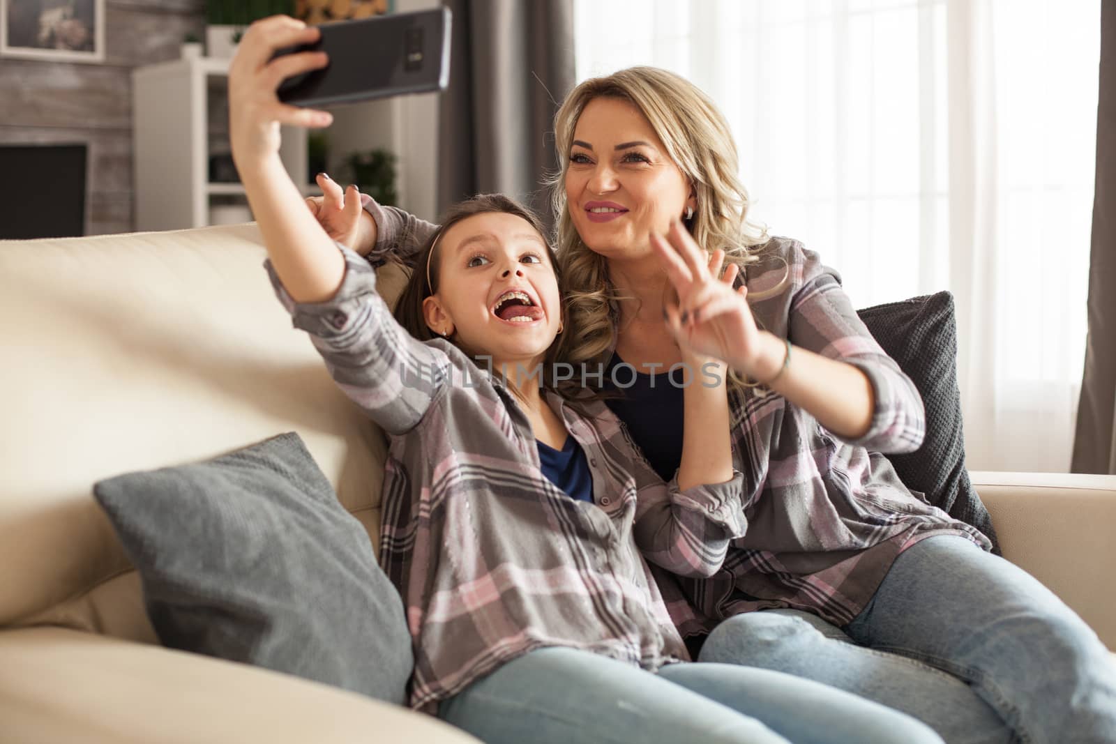 Funny little daughter and her mother are taking a selfie using smartphone. Happy kid.