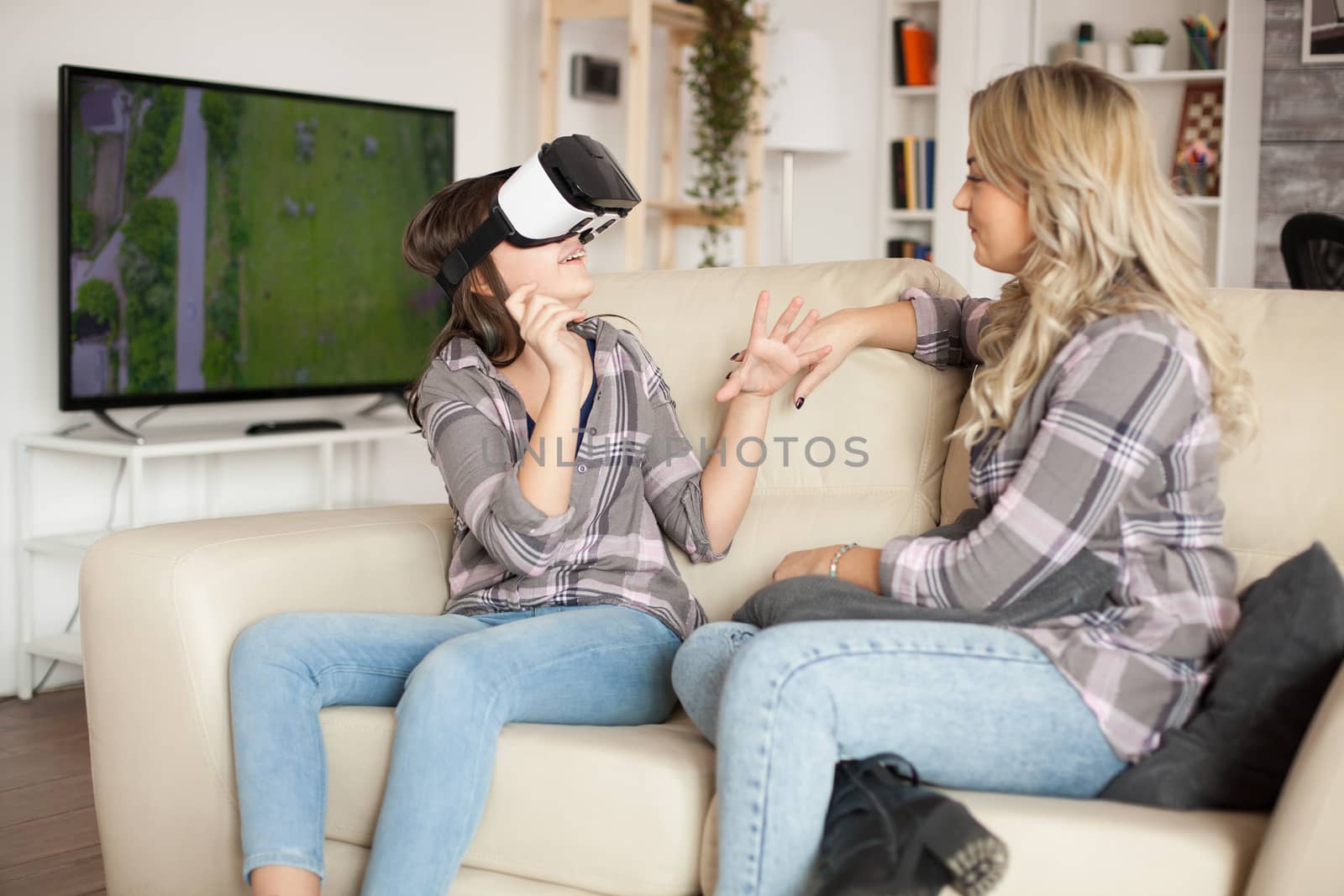 Happy little girl wearing virtual reality headset while sitting on the couch with her mother.