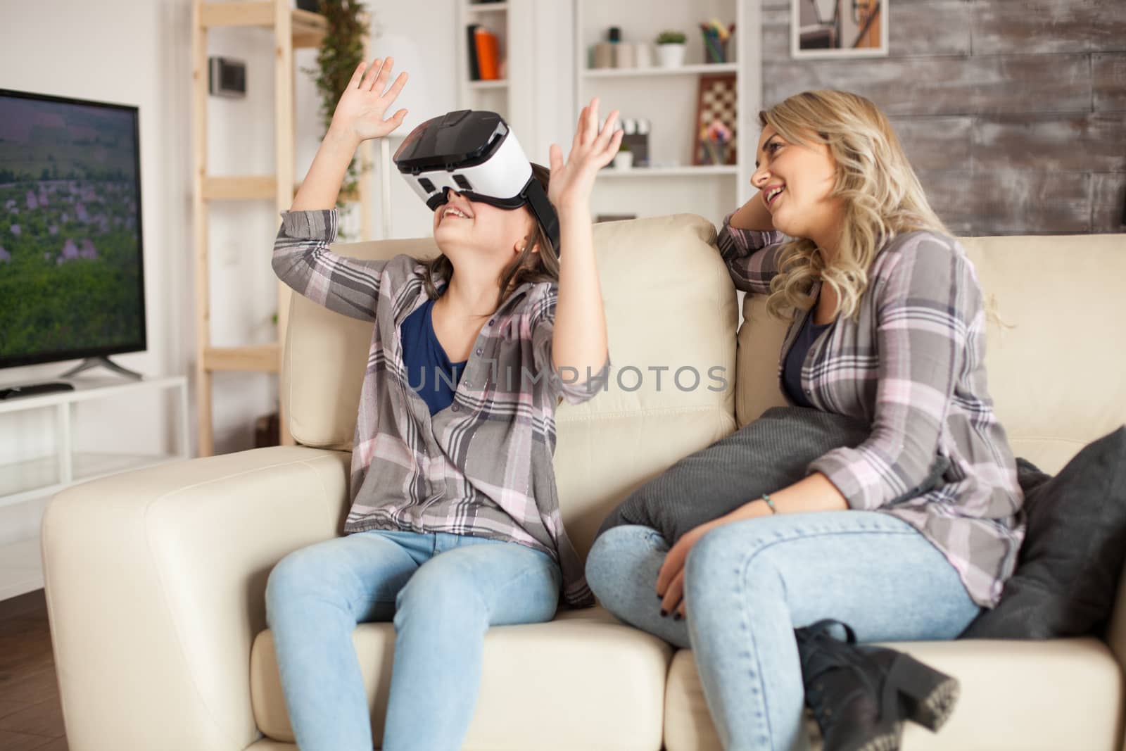 Amazed little girl sitting next to her mother on the couch while using virtual reality headset.