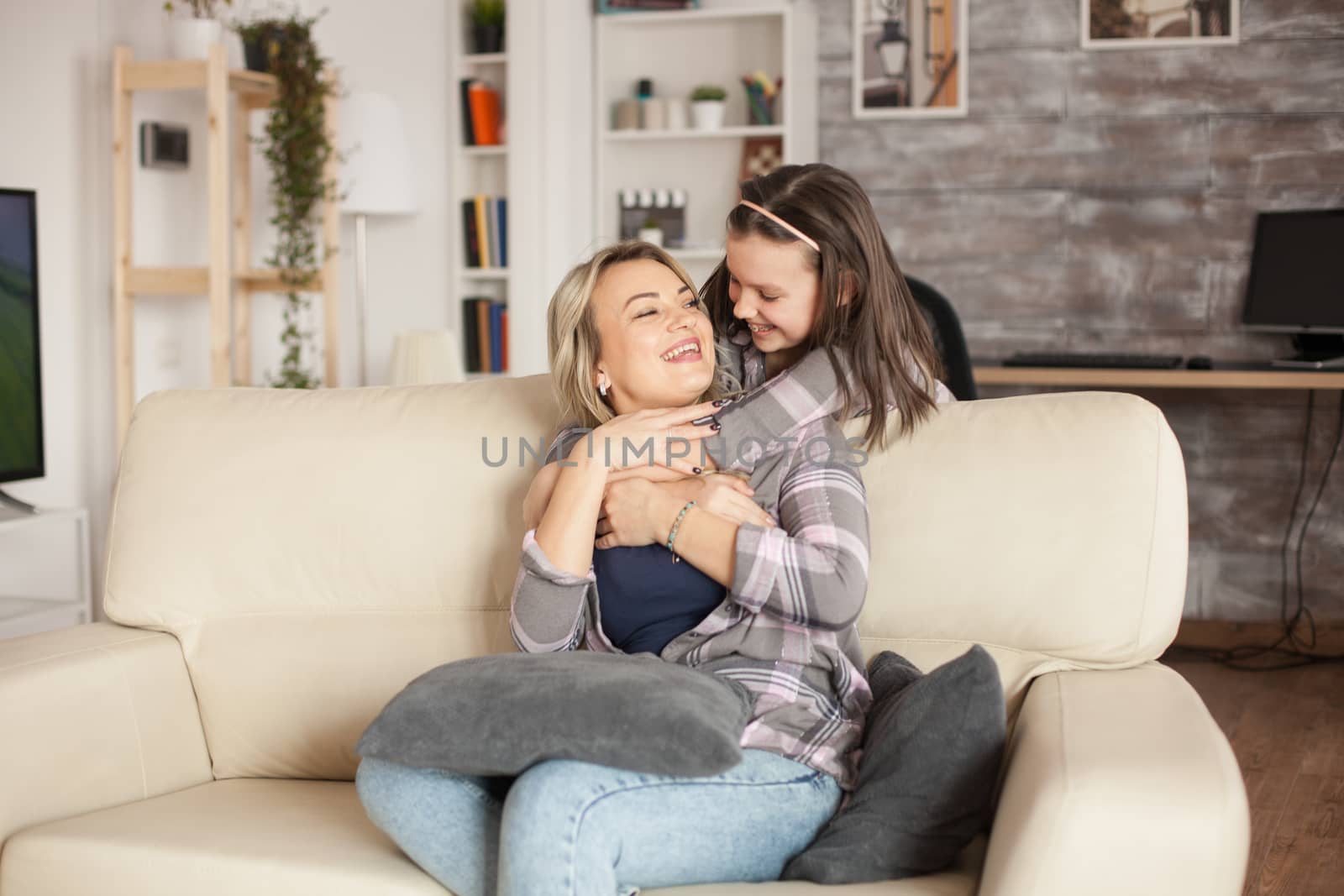 Young mother sitting on the couch hugged from behind by her little daughter with braces. Happy childhood.
