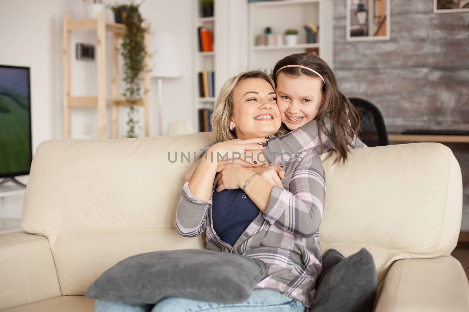 Little girl with braces showing her affection to her mother by hugging her from behind.