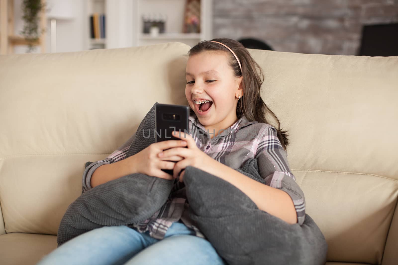 Happy little girl sitting on the couch in living room taking a selfie.