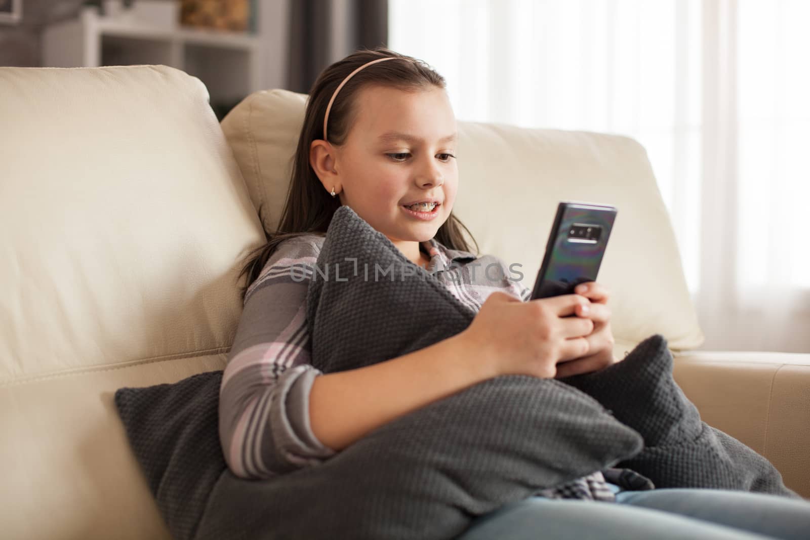 Little girl sitting on the couch in living room texting on smartphone.