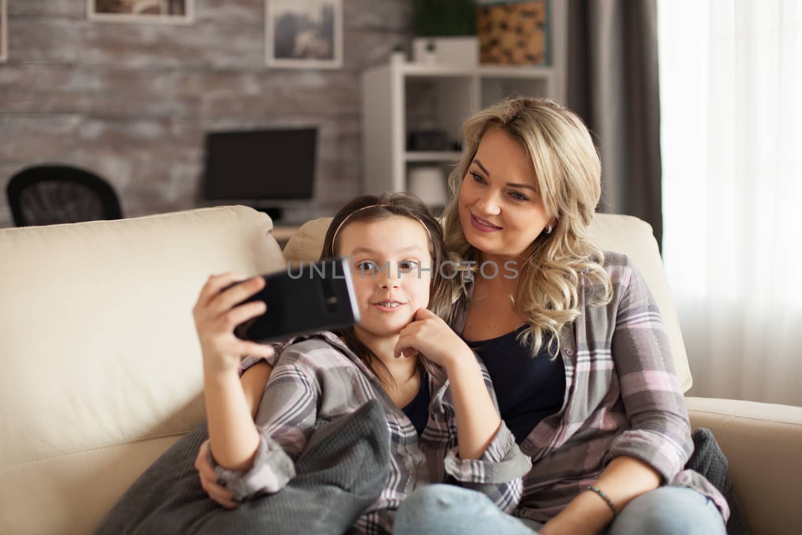 Preschool girl with her mum having a video call with grandparents sitting on the couch. Modern mum.