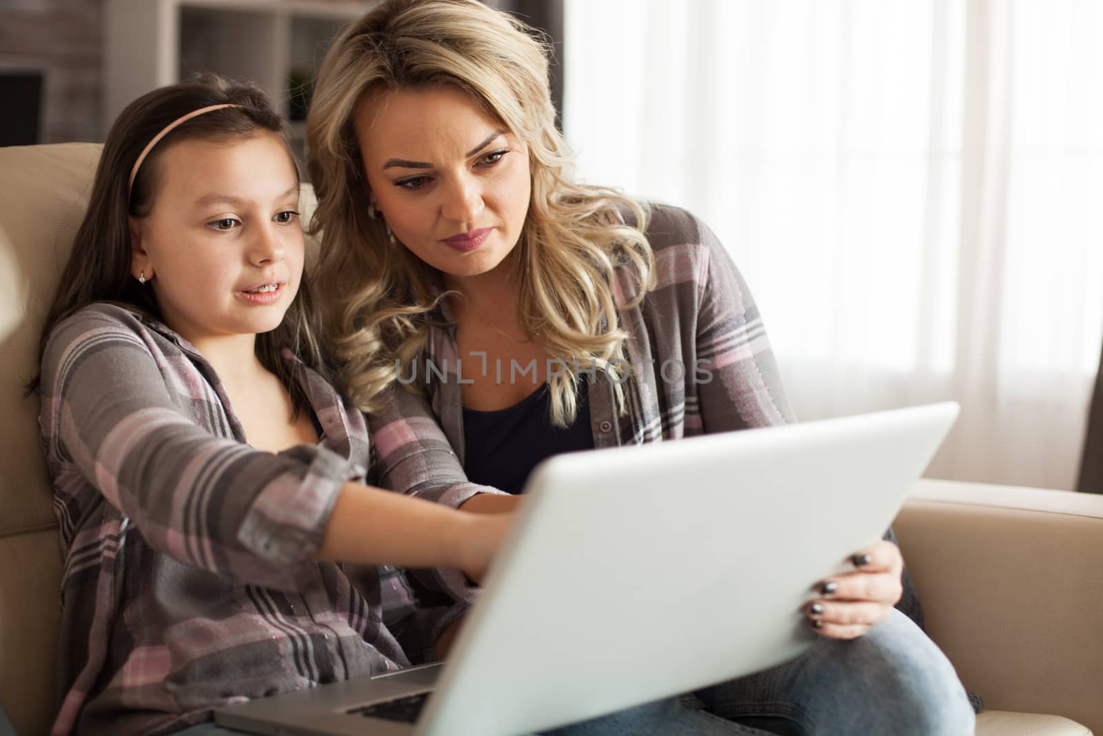 Mother and daughter sitting on the couch in living room by DCStudio