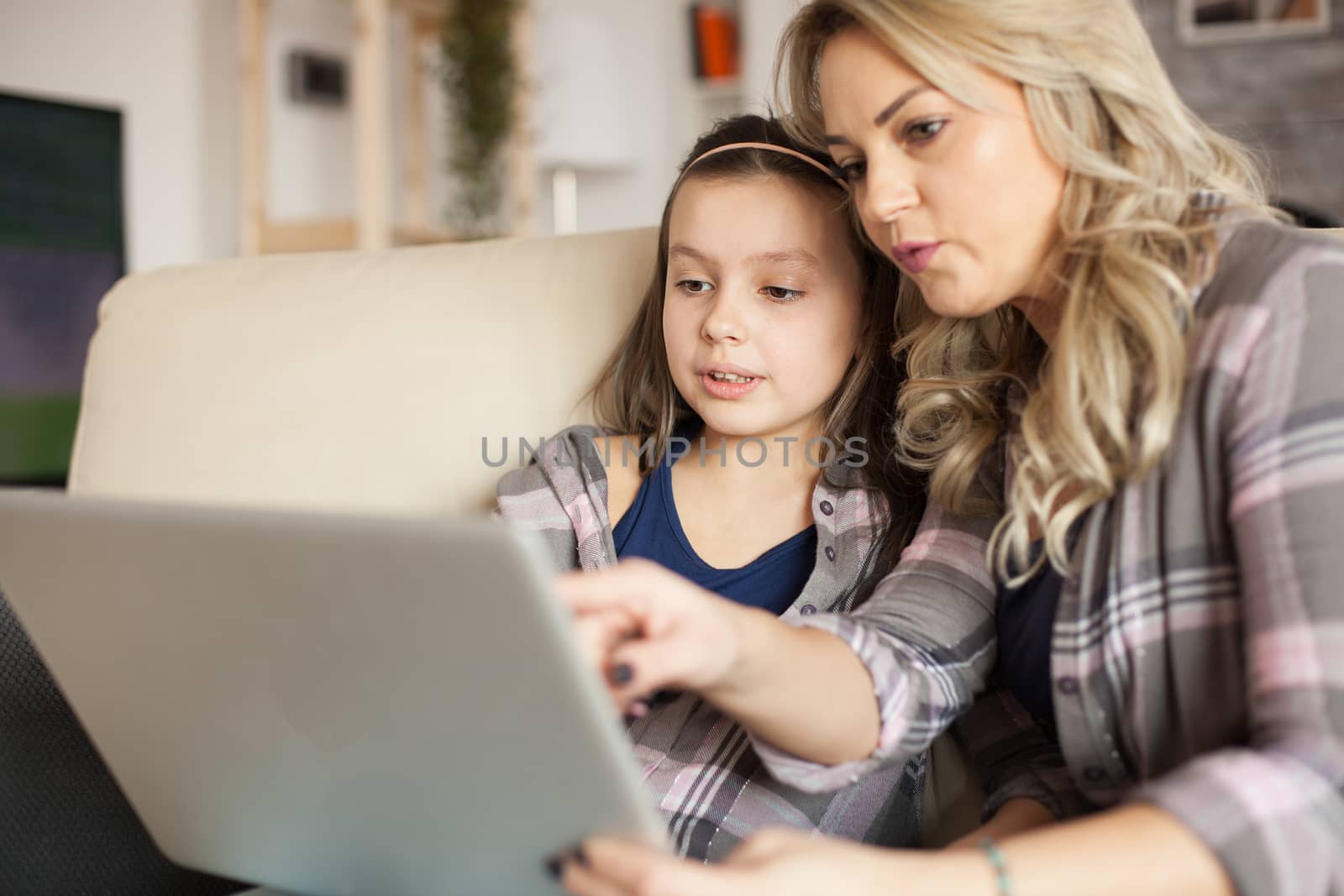 Young mother pointing at laptop while surfing on the internet with her daughter