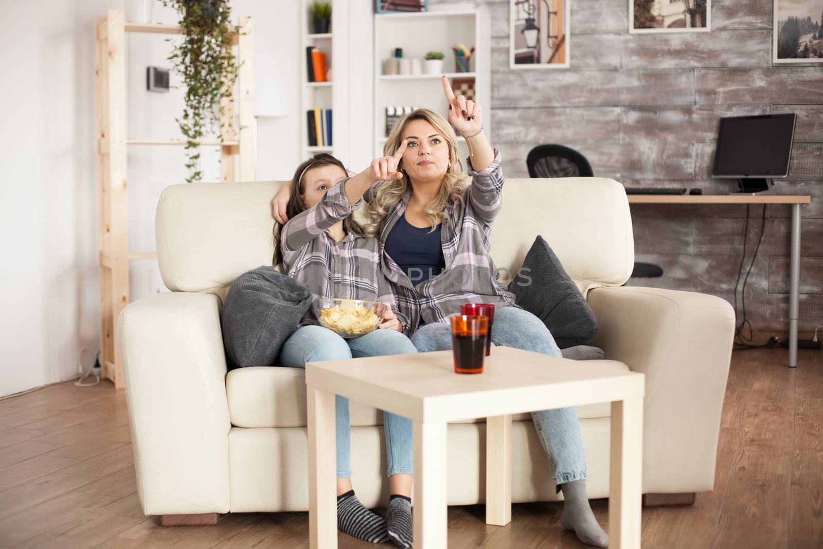 Young mother and daughter sitting on the couch using augmented reality to change tv channel.
