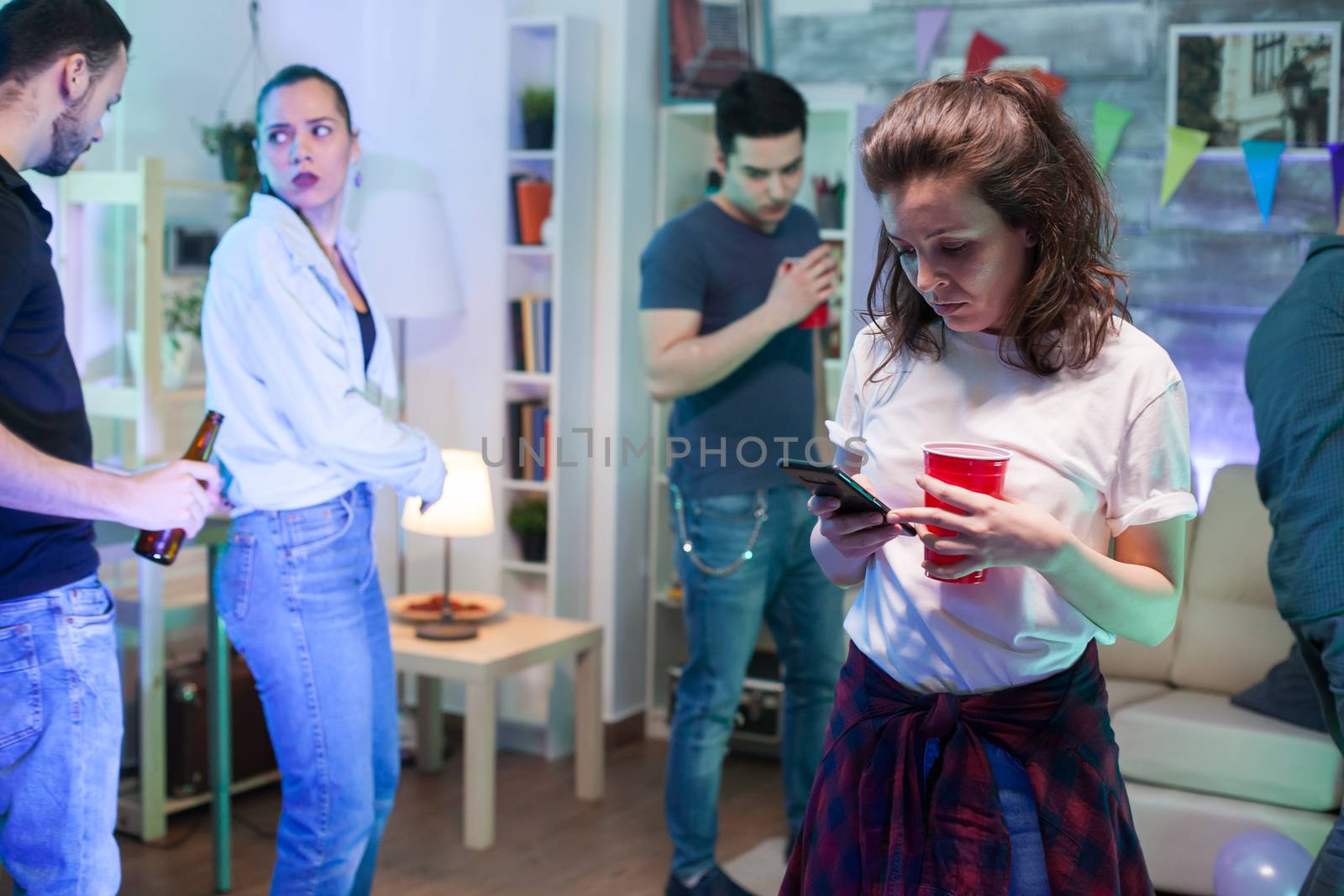 Attractive young woman using smartphone while her friends are dancing in the background.