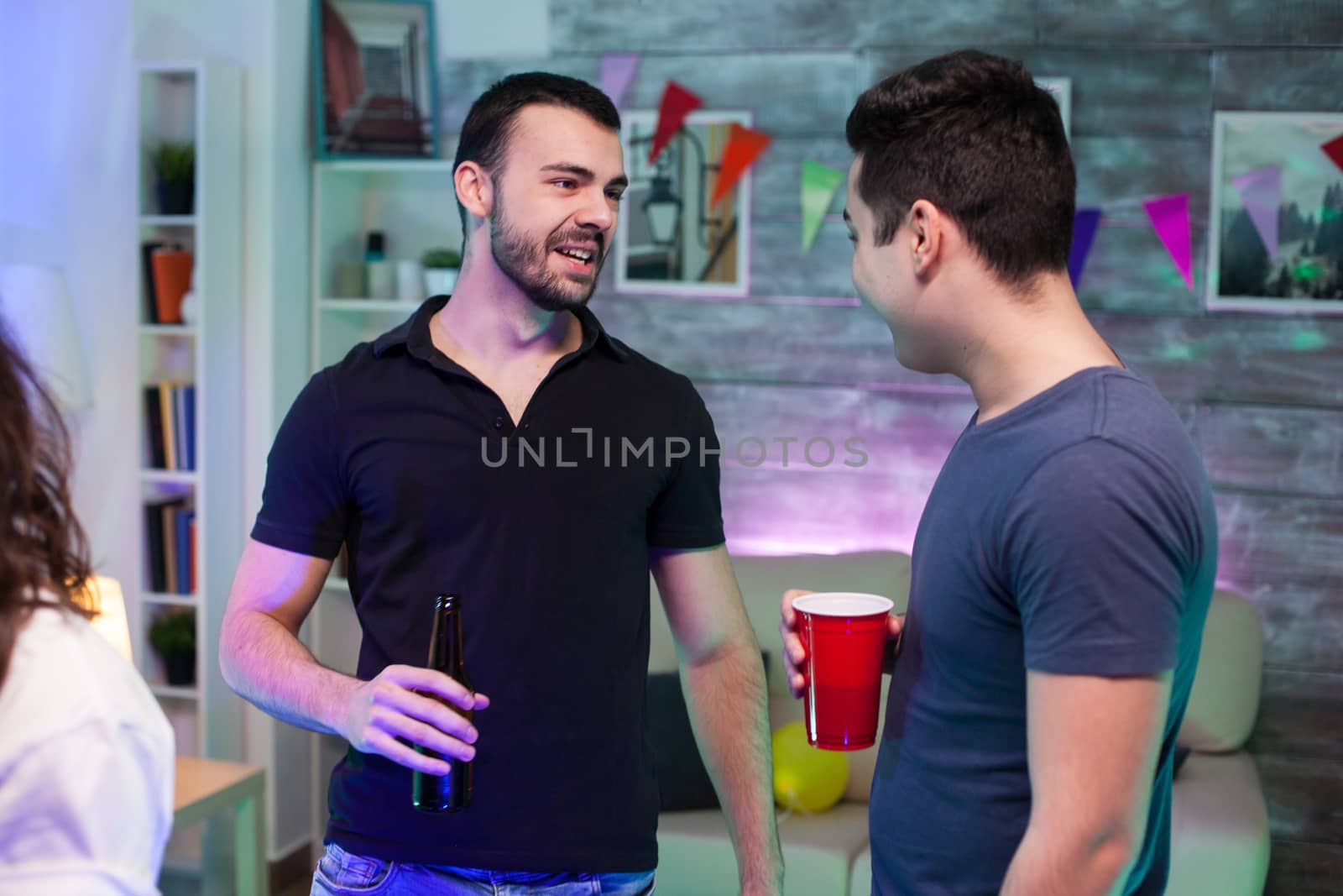 Attractive bearded man holding a beer at a party and talking with his friend.