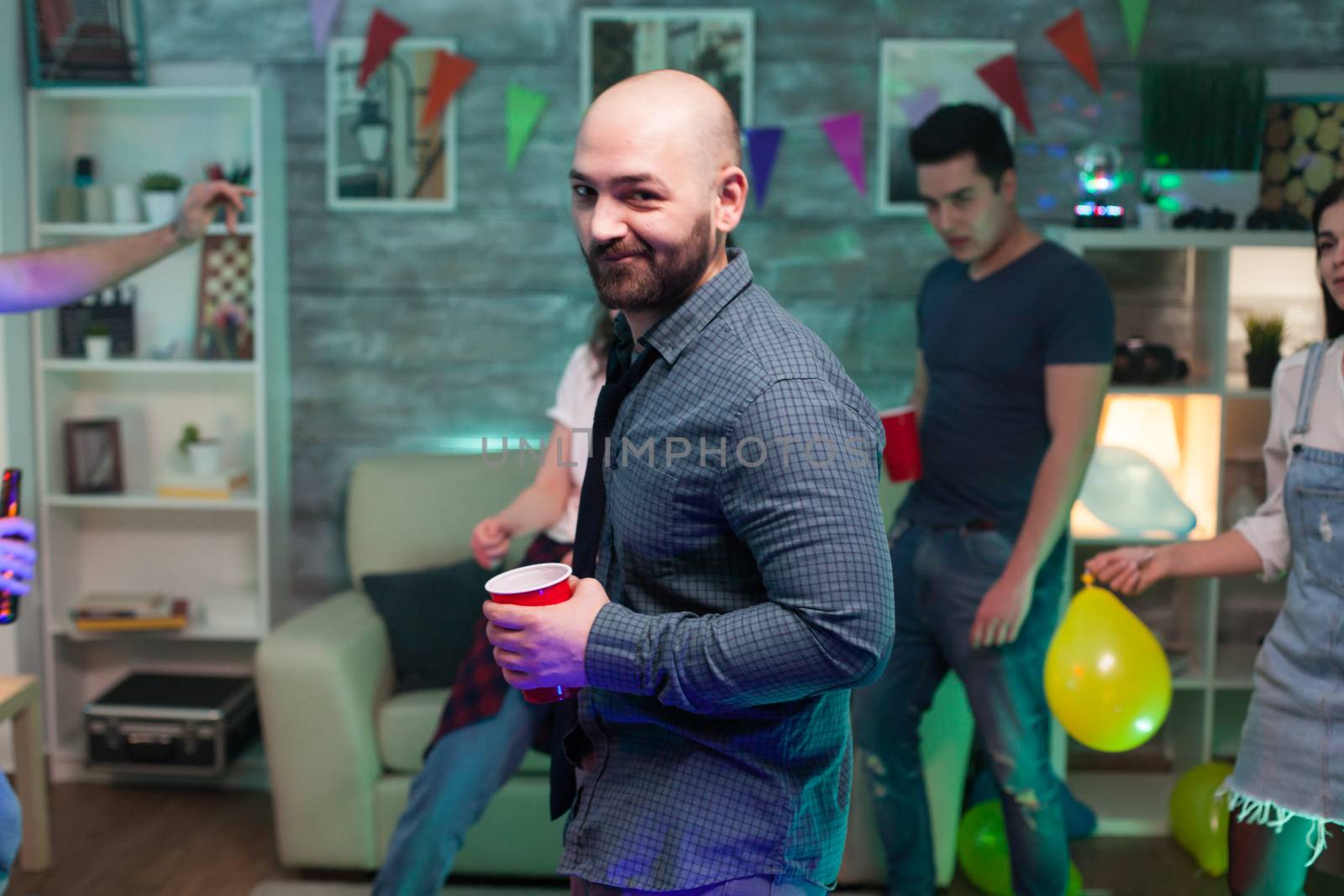 Bald man looking at the camera at a party his friends while partying. Man standing with a beer cup.