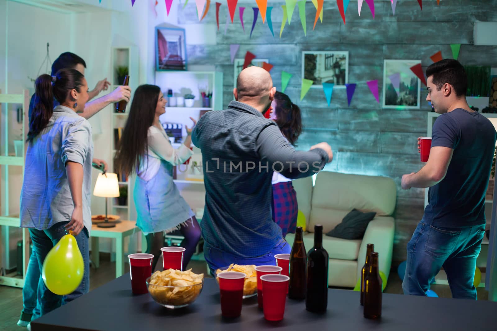 Back view of man dancing with his friends having a good time partying. Chips and balloons.