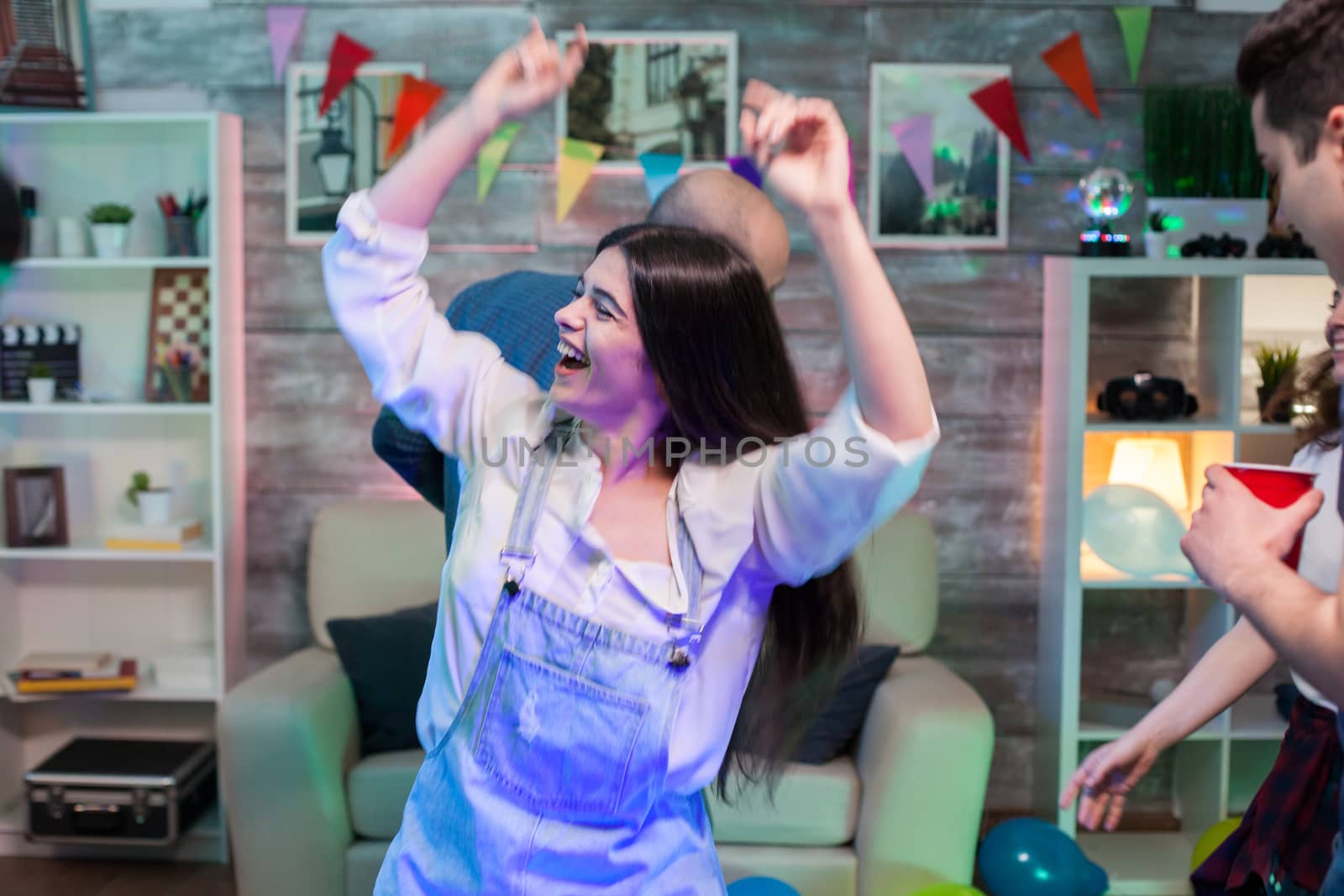 Excited young woman dancing at a party with her friends on disco music.