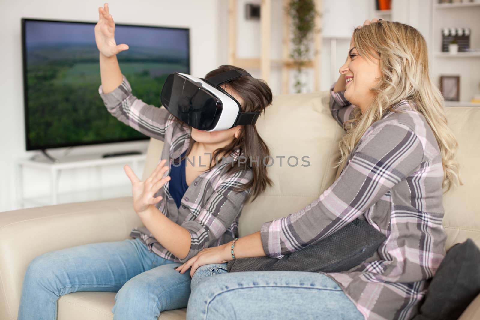 Beautiful mother laughing while her daughter is playing games using virtual reality headset.