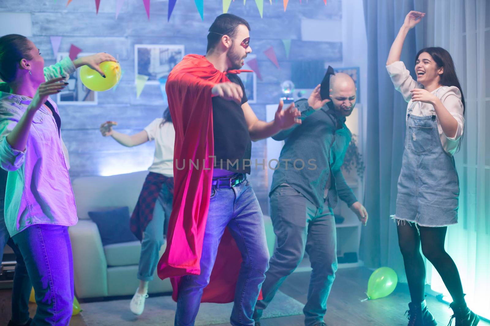 Group of friends enjoying their time at a party in a room with neon lights. Man in superhero costume.