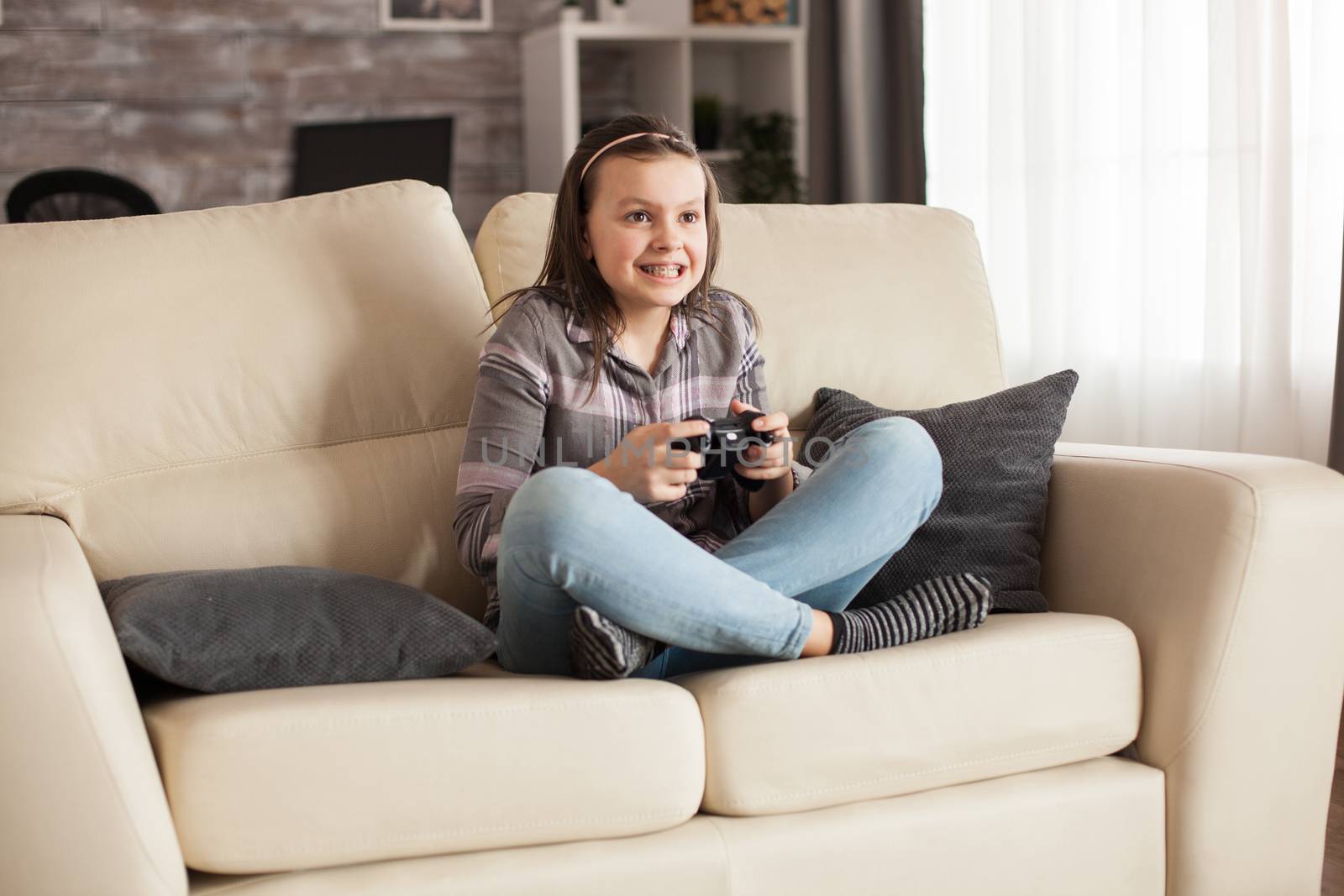 Focused little girl with braces playing video games using wireless joystick.