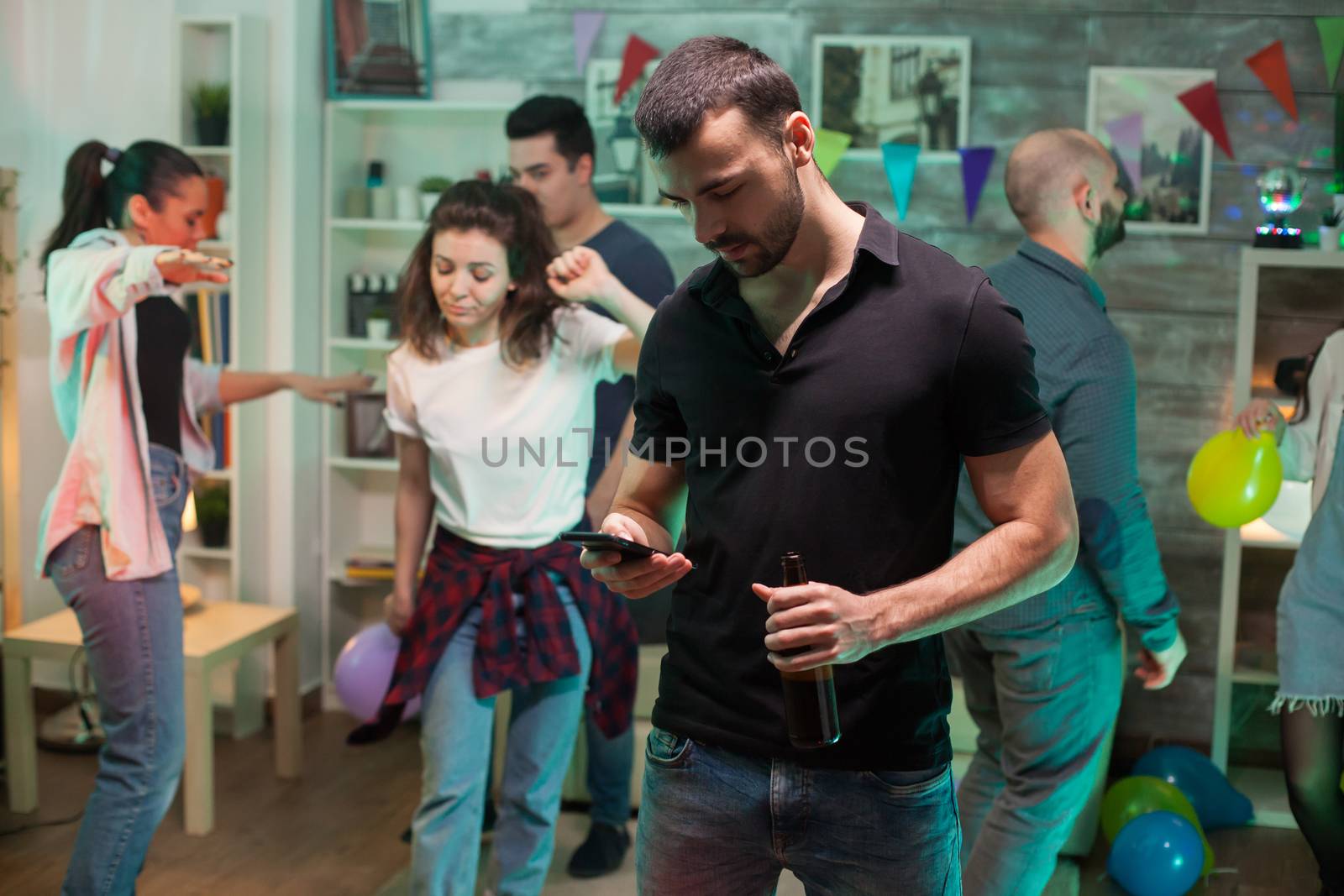 Young man browsing on his mobile phone at a party with disco music.