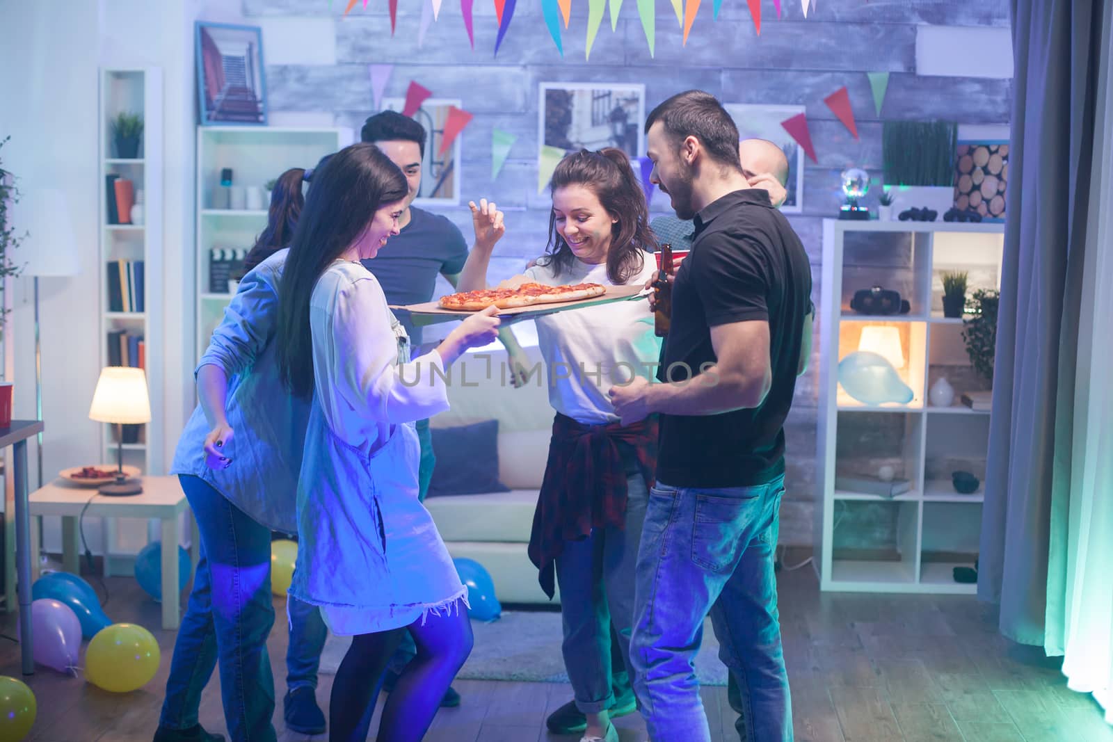 Young woman arriving at the party with delicious pizza at the party for her friends.