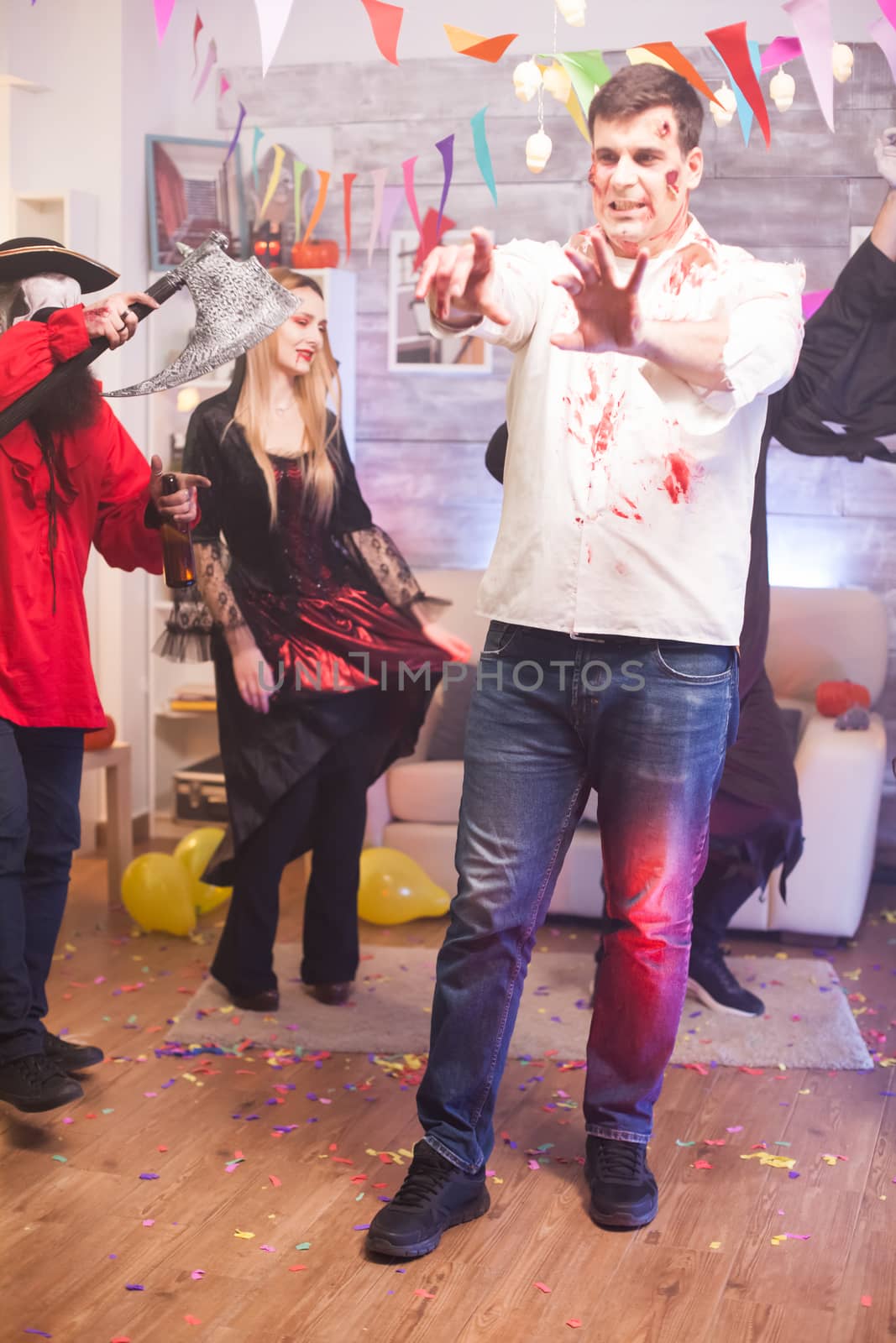 Man wearing a zombie costume with creepy expression at halloween celebration with his friends.