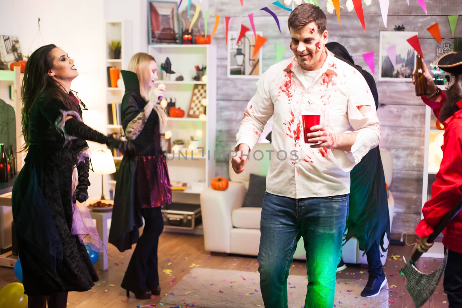 Man dressed up like a zombie drinking beer while celebrating halloween with his friends.