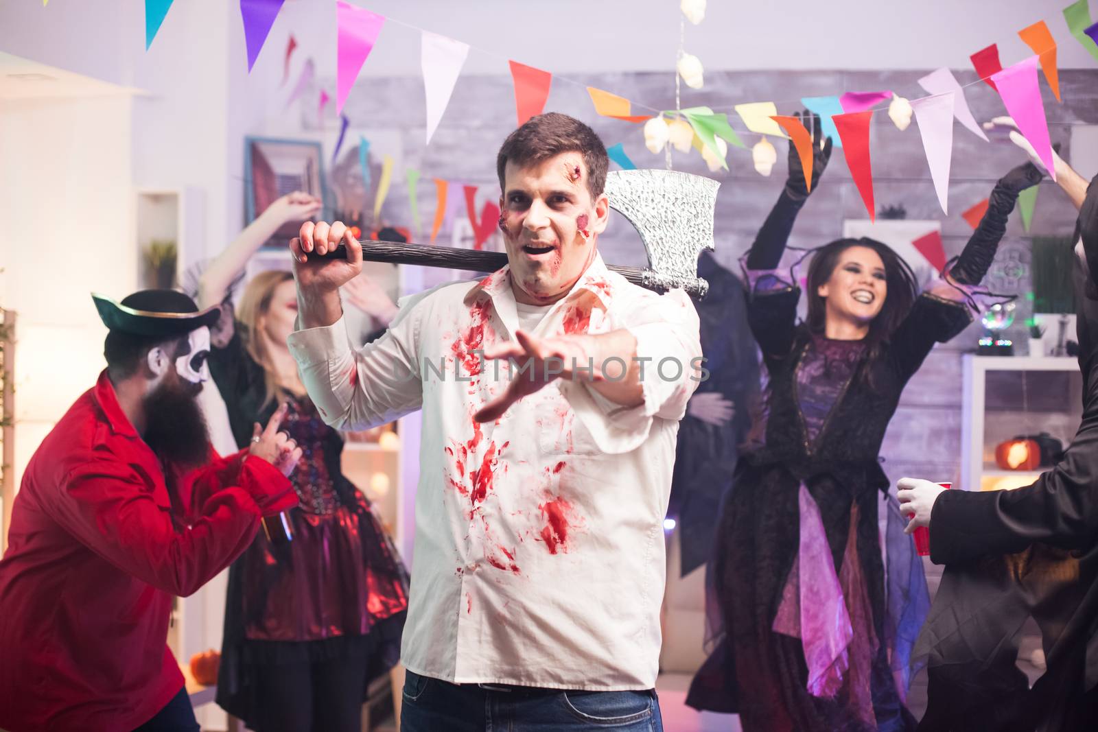 Man dressed up like a spooky zombie holding an axe at halloween party.