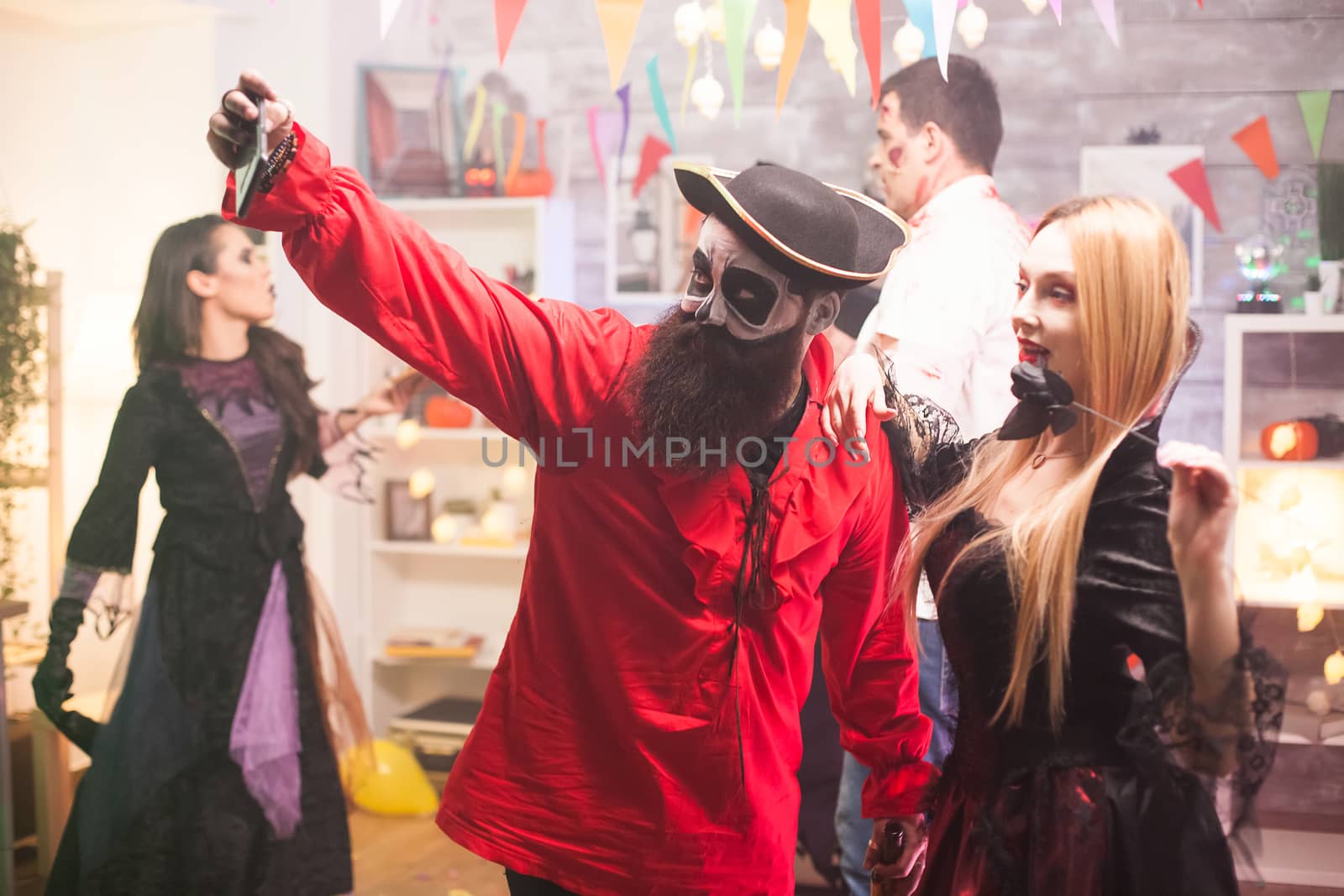 Attractive man and woman dressed up like pirate and vampire taking a selfie at halloween party.