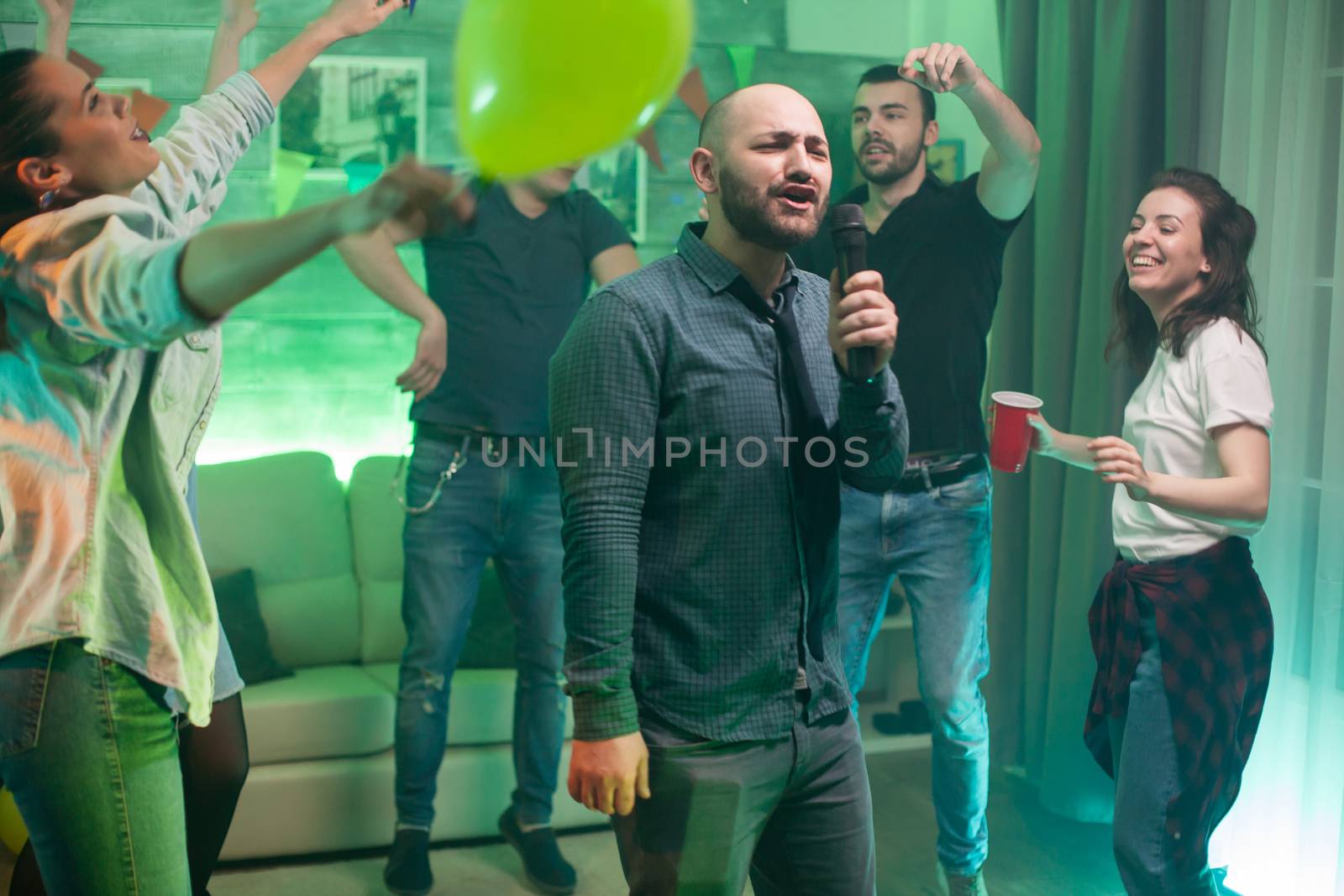 Cheerful bald man doing karaoke for his friends at the party.