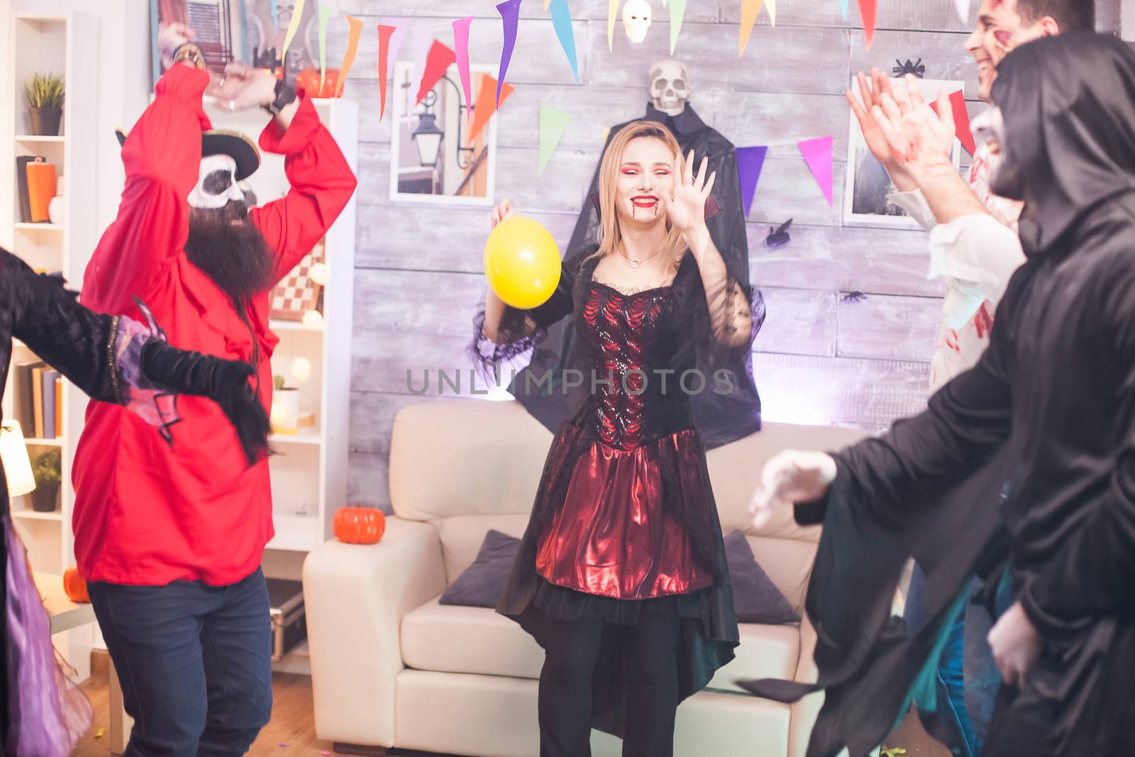 Cheerful vampire woman with bloody lips dancing with hands up at halloween celebration.