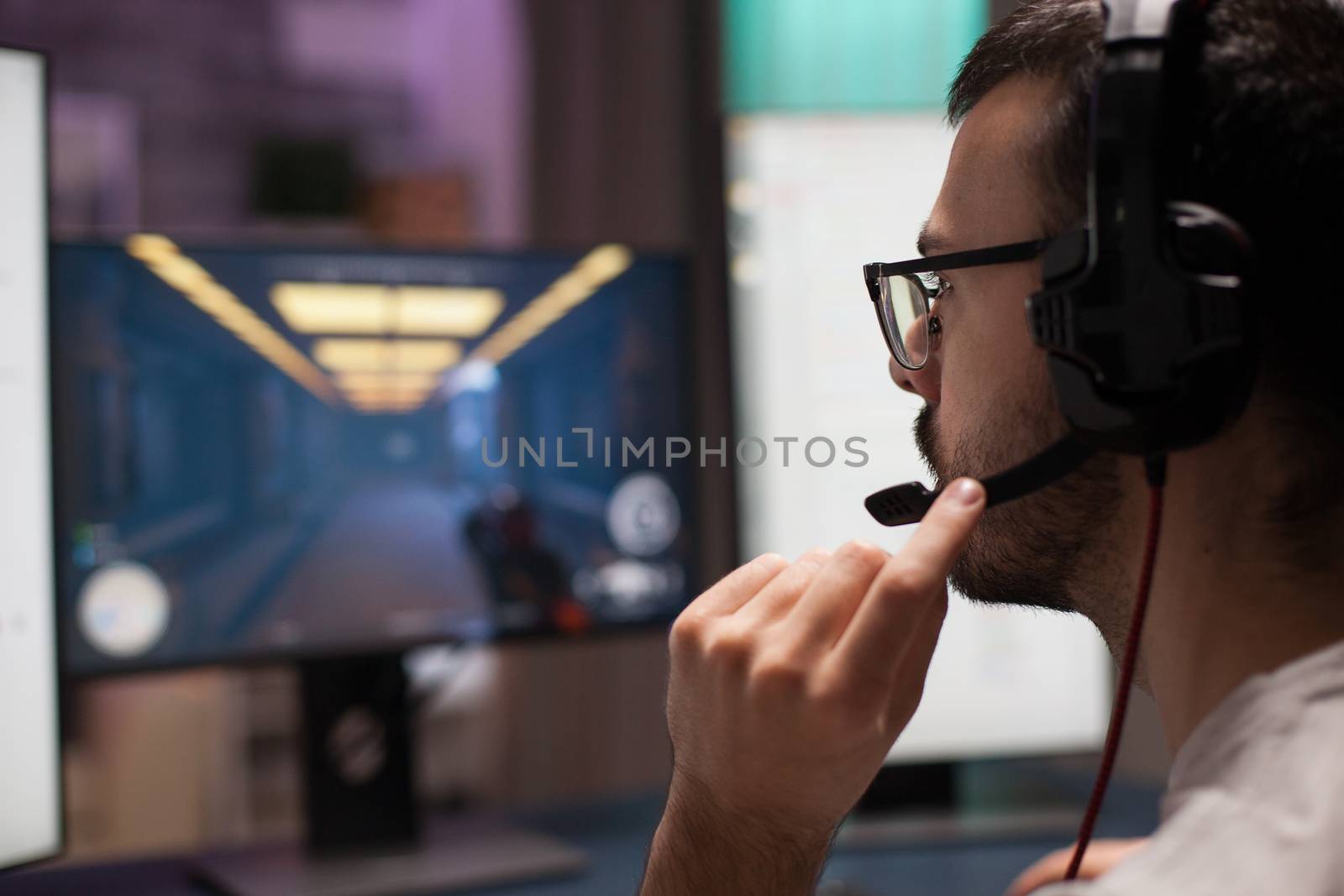 Competitive young man playing shooter video games wearing headphones in a room with neon light.