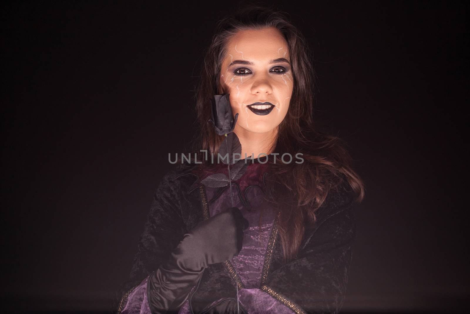 Evil and scary female witch over black background with a rose. Halloween costume.