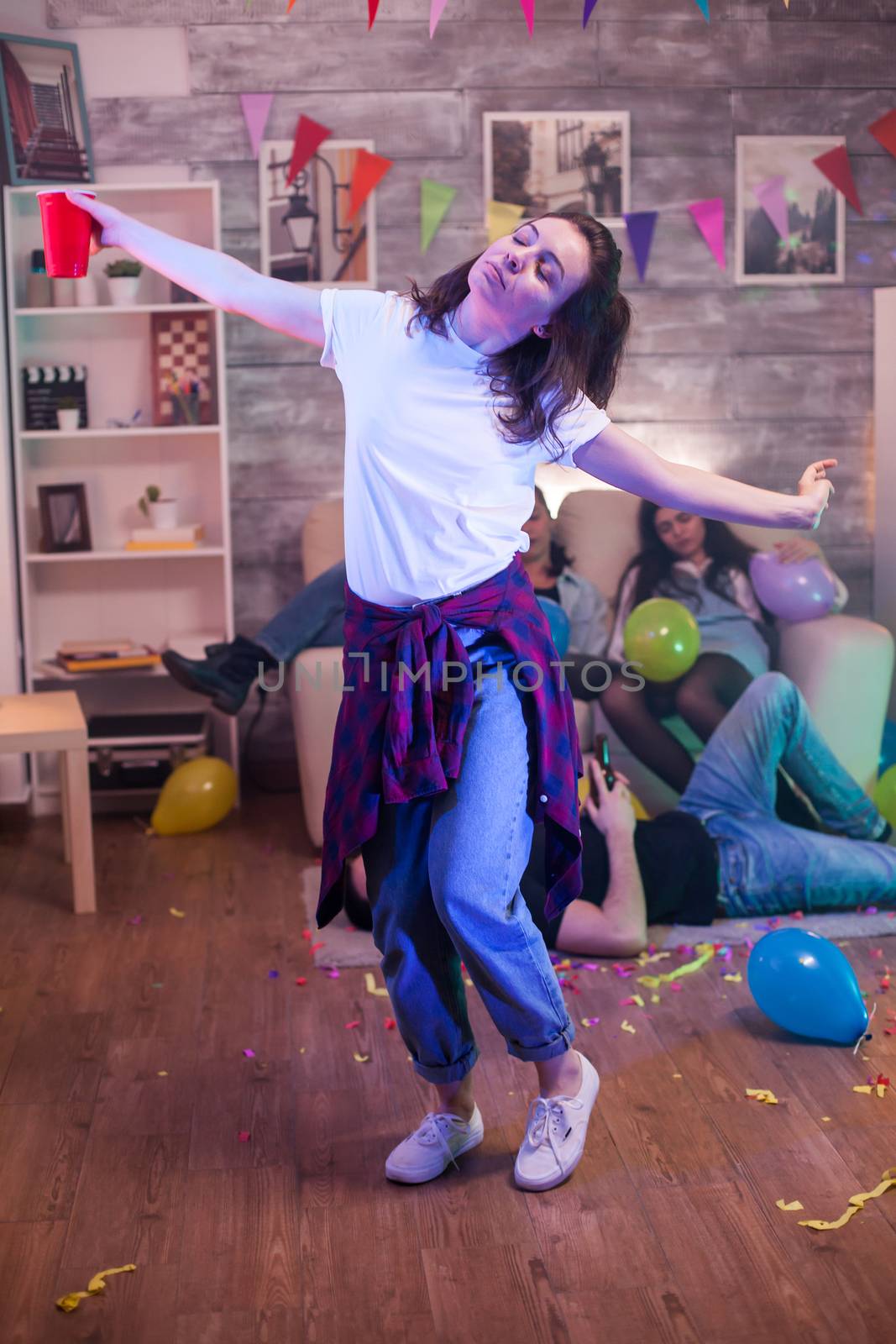 Cheerful caucasian woman dancing alone at her friends party holding a beer cup.