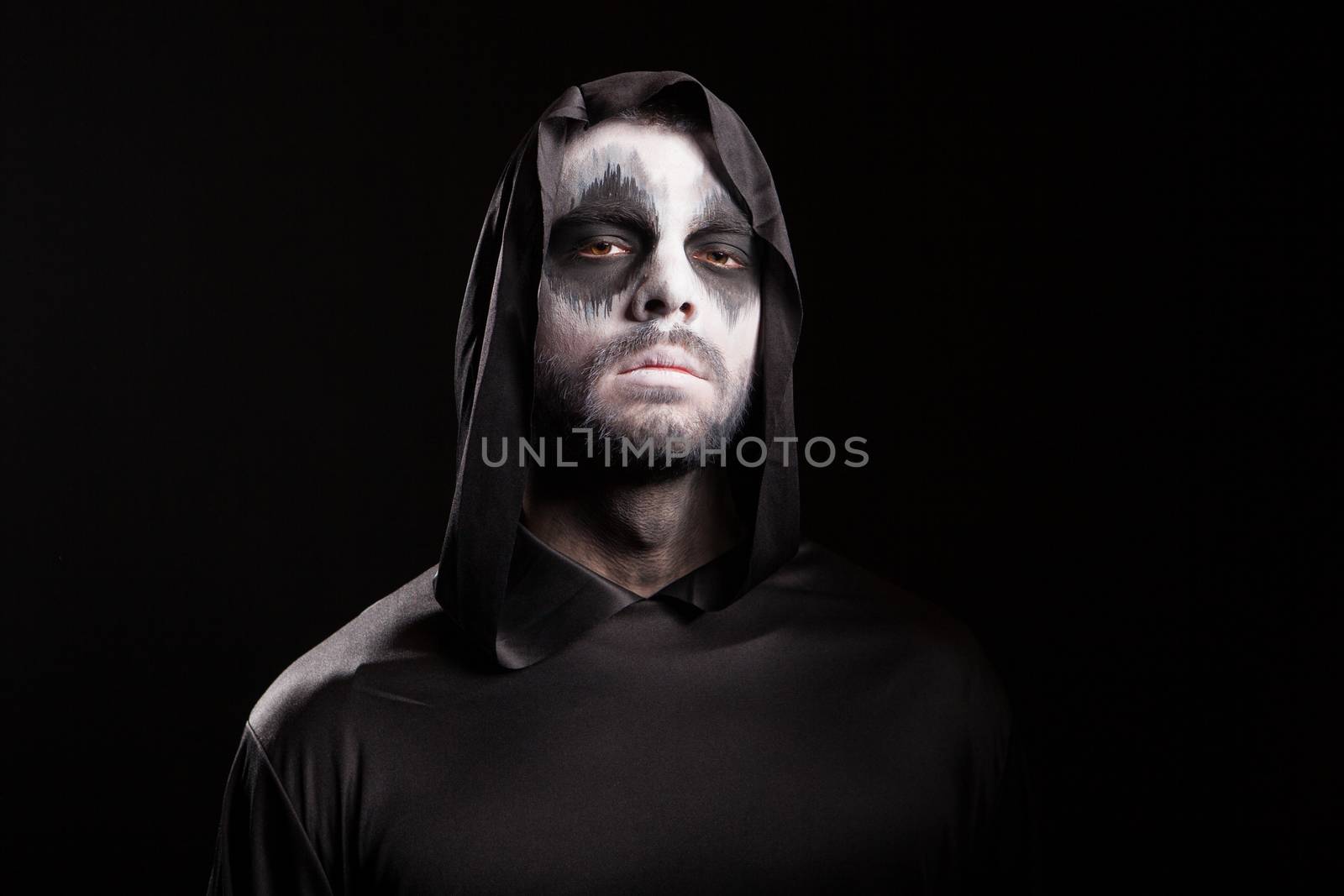 Man with creepy face dressed up like grim reaper over black background.